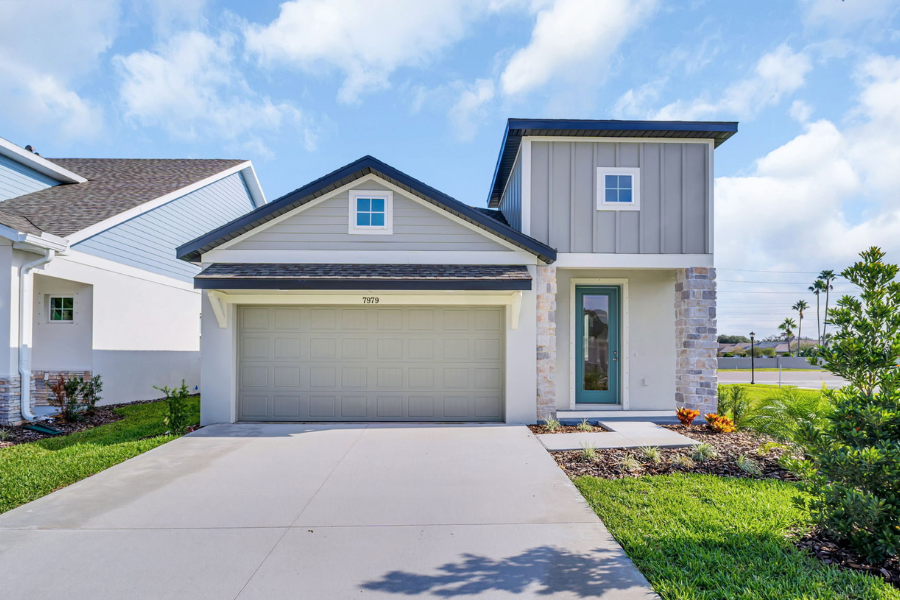New-construction two-story home with light gray siding, board-and-batten accents, stone trim, a two-car garage, and a landscaped front yard under a blue sky.